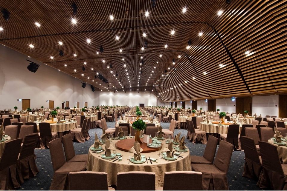 Không gian sảnh tiệc cưới Gem Center Castor và Pollux với bàn tròn nâu, ánh sáng vàng tại trung tâm Quận 1