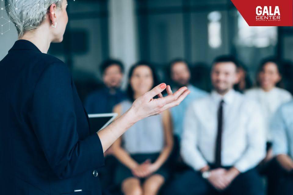 Kh&aacute;ch mời ngồi nghe thuyết tr&igrave;nh trong ph&ograve;ng họp hiện đại, đồng bộ trang phục c&ocirc;ng sở chuy&ecirc;n nghiệp